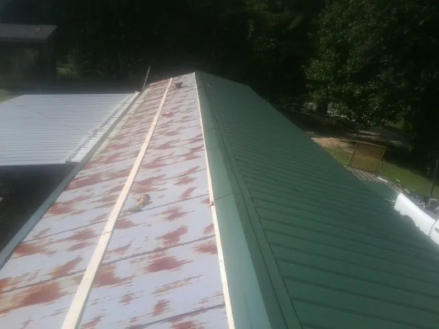 Old rusted panels beside newly installed green metal roofing — Wind Damage Roof Repair by Roofing Brothers in Randall